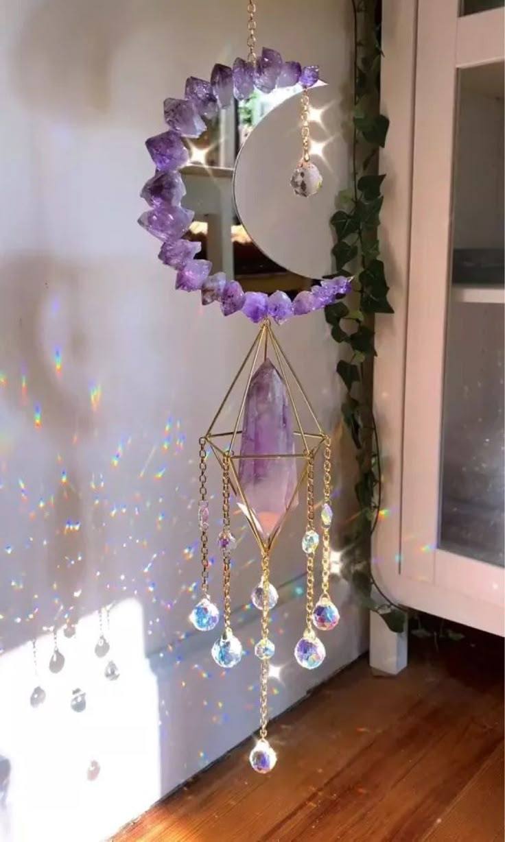 a purple and white wind chime hanging from a wall next to a window with light shining on it