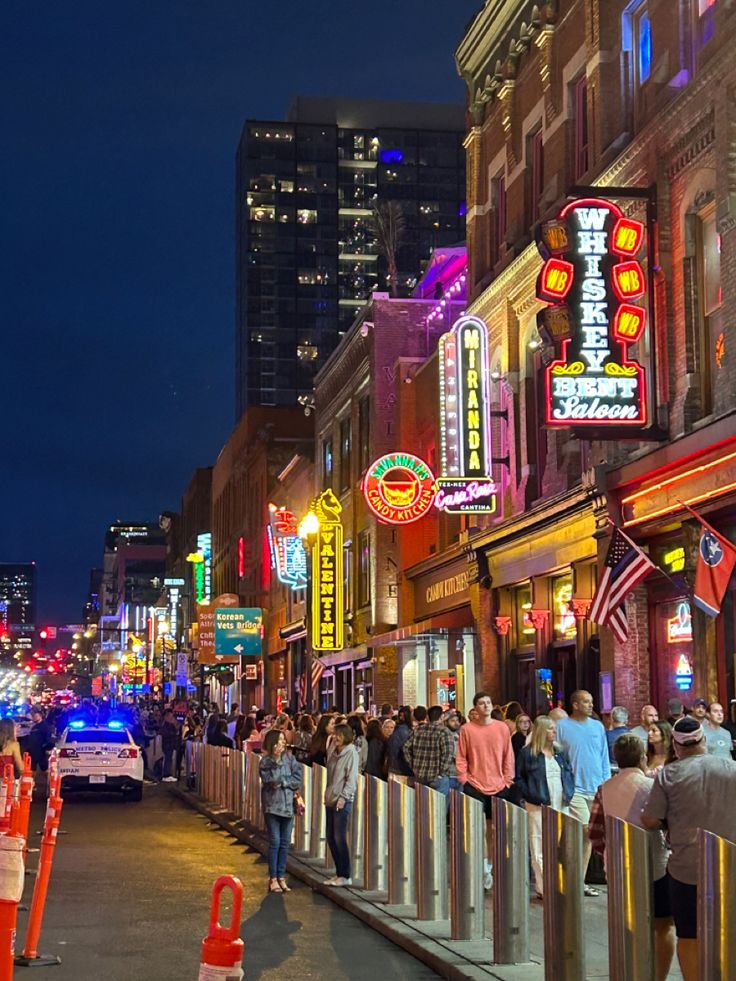 a crowd of people standing on the side of a road next to tall buildings at night