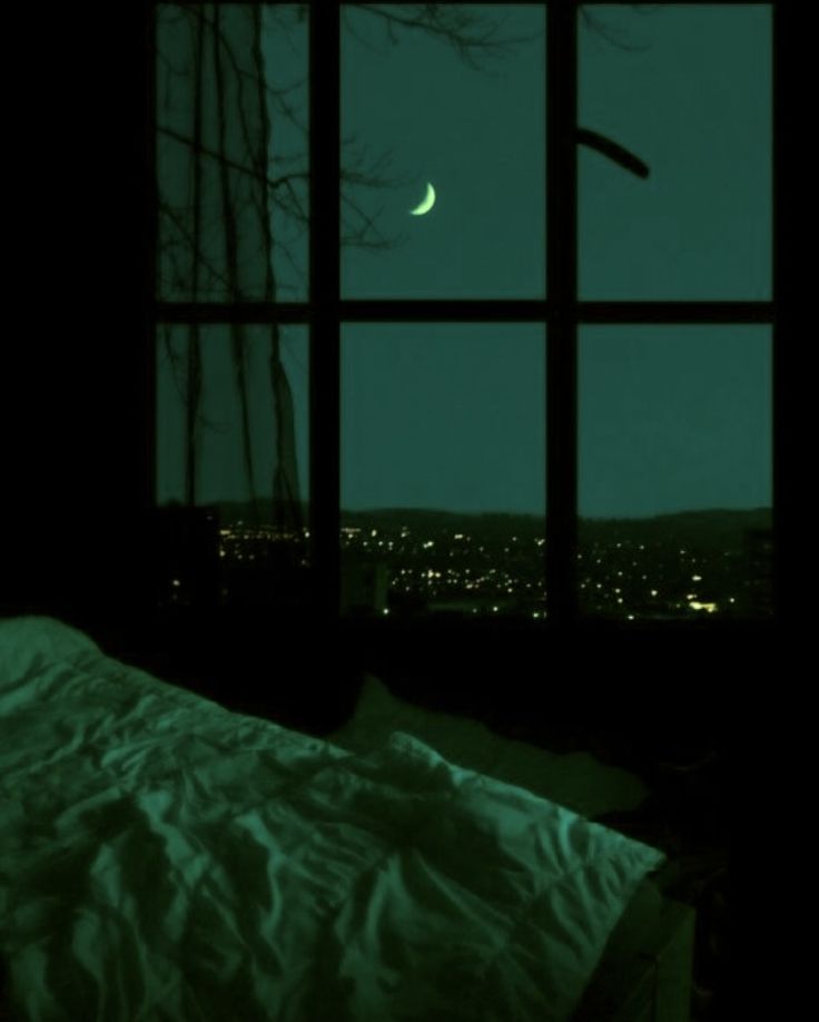 a bed sitting under a window next to a night sky