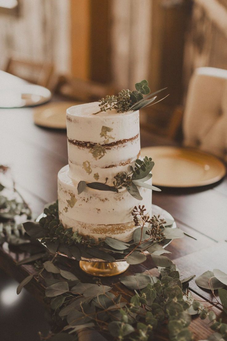 a white wedding cake with greenery on the top is sitting on a wooden table