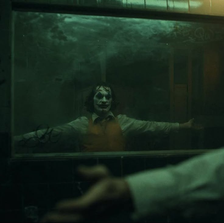 the joker is looking at himself in the mirror while he's holding his hands out