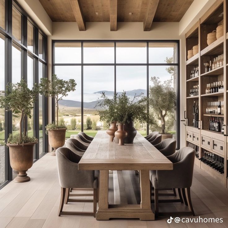 the dining room table is surrounded by chairs and potted plants in front of large windows