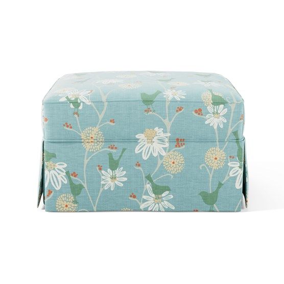 a blue ottoman with white flowers and green leaves on the top, sitting in front of a