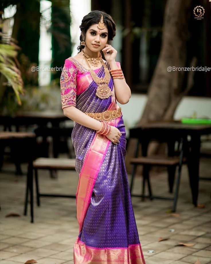 a woman in a purple and pink saree talking on a cell phone while standing next to a tree