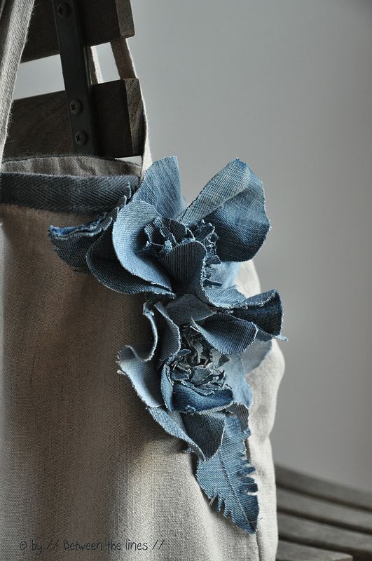 a blue flower is attached to the back of a canvas bag on a wooden bench