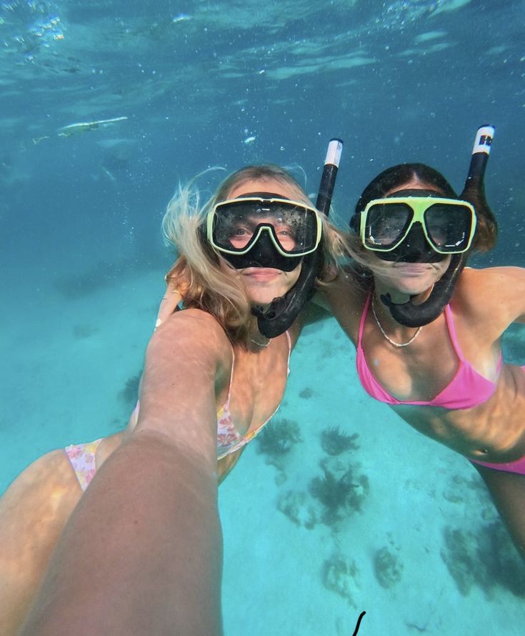 two women wearing goggles and snorkels are swimming in clear blue water