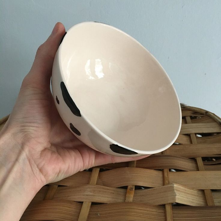 a hand is holding a white bowl with black spots on the rim and it's in front of a wicker basket