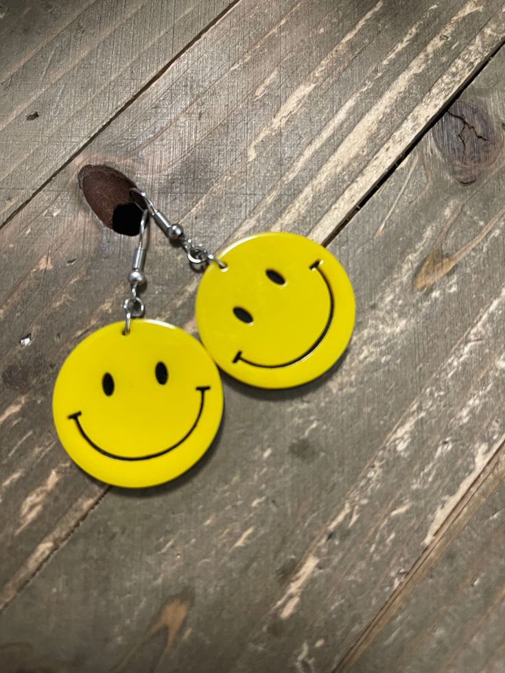 two yellow smiley face key chains hanging from a wooden table with wood planks behind them