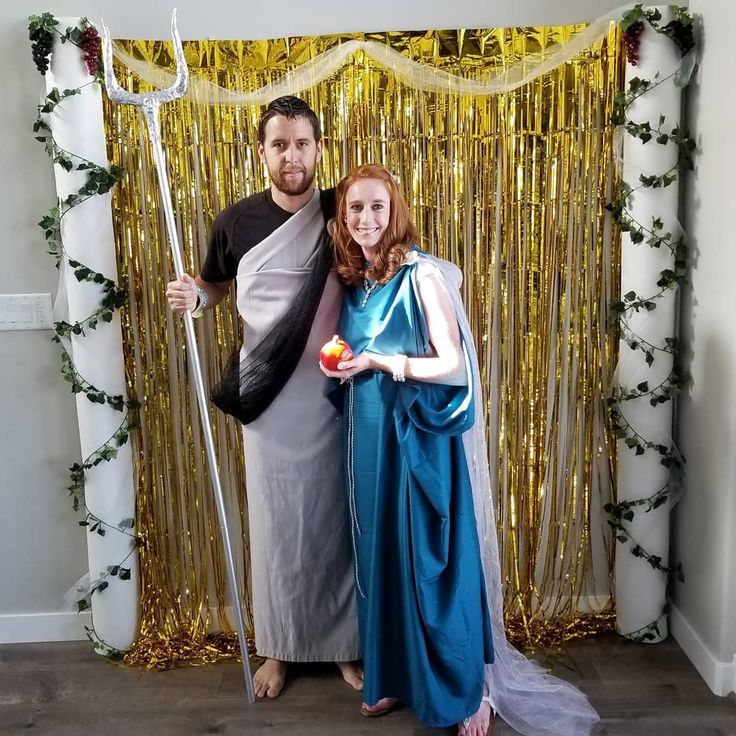 a man and woman pose for a photo in front of a backdrop with gold streamers