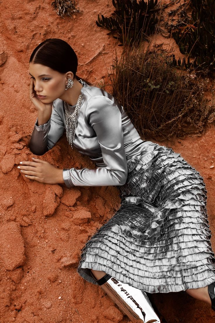 a woman laying on the ground with her hand under her chin, wearing a silver dress