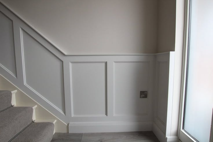 an empty room with white walls and gray carpeted stairs leading up to the second floor