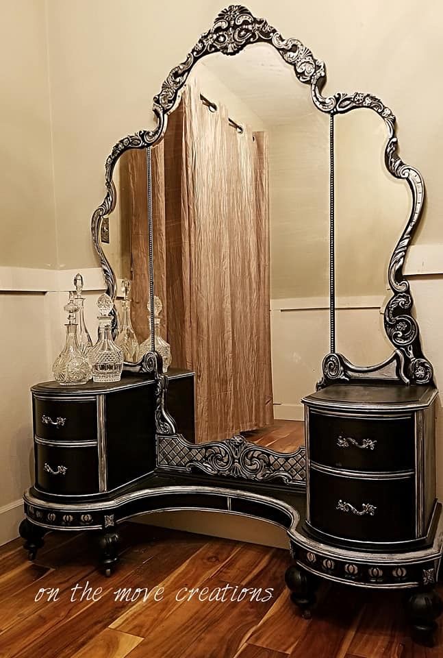 an ornate black and silver dresser with mirror on it's side, in front of a wooden floor