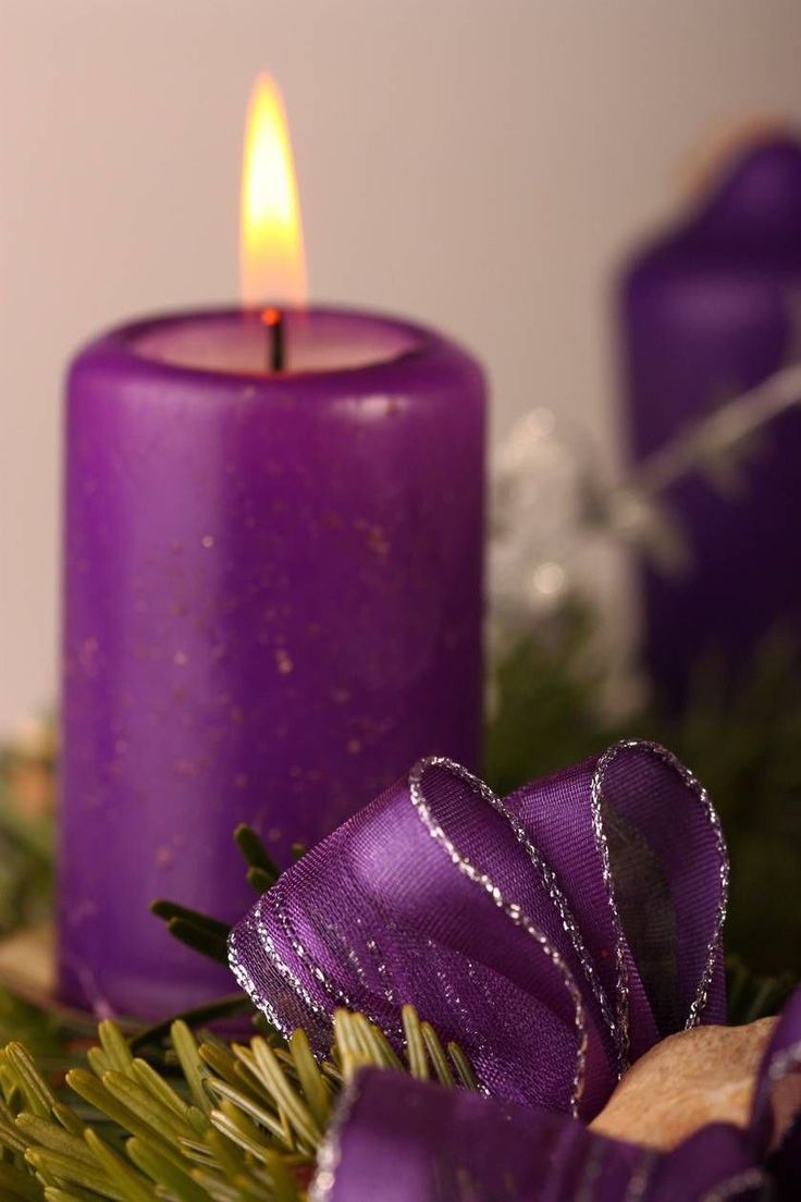 a purple candle sitting on top of a table next to some green leaves and other decorations