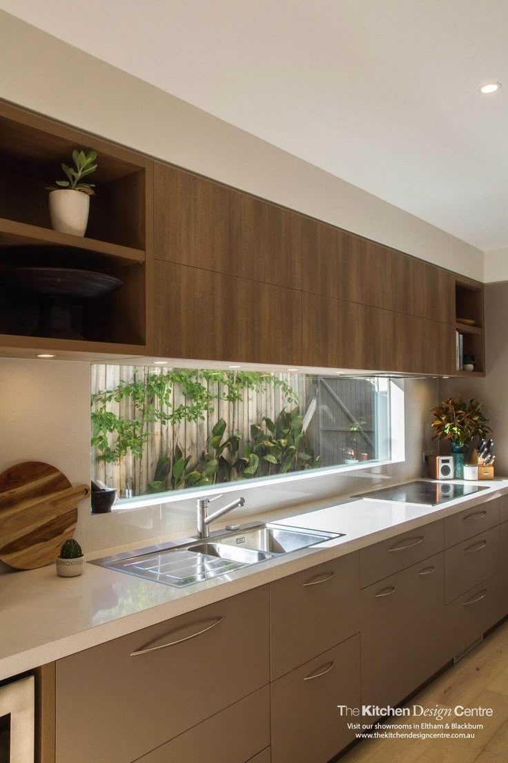 a kitchen with wooden cabinets and white counter tops, plants on the window sill