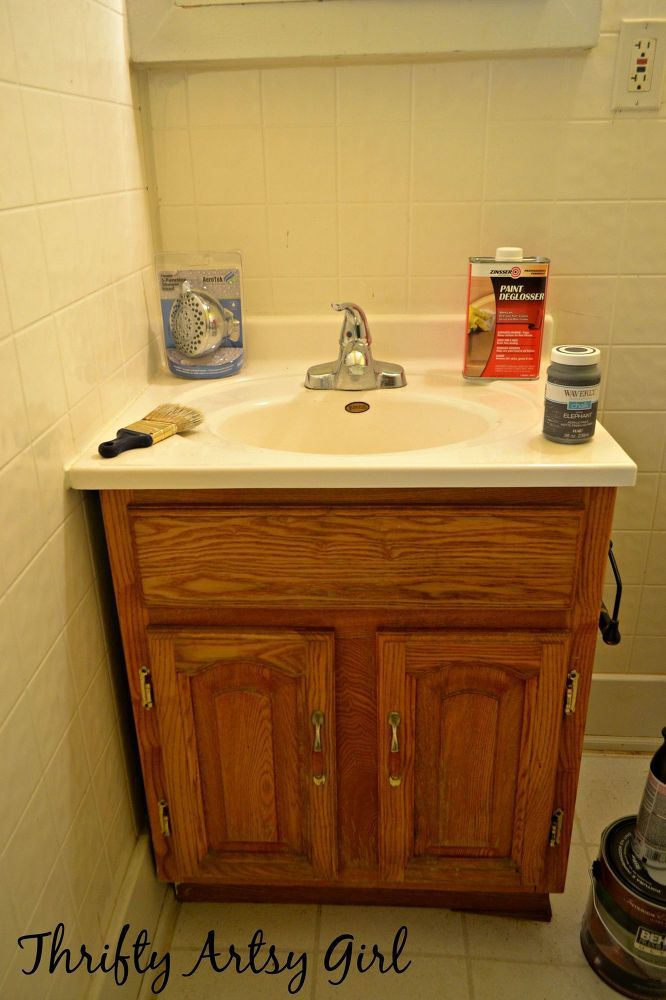 a bathroom sink sitting under a window next to a white tiled wall and wooden cabinets