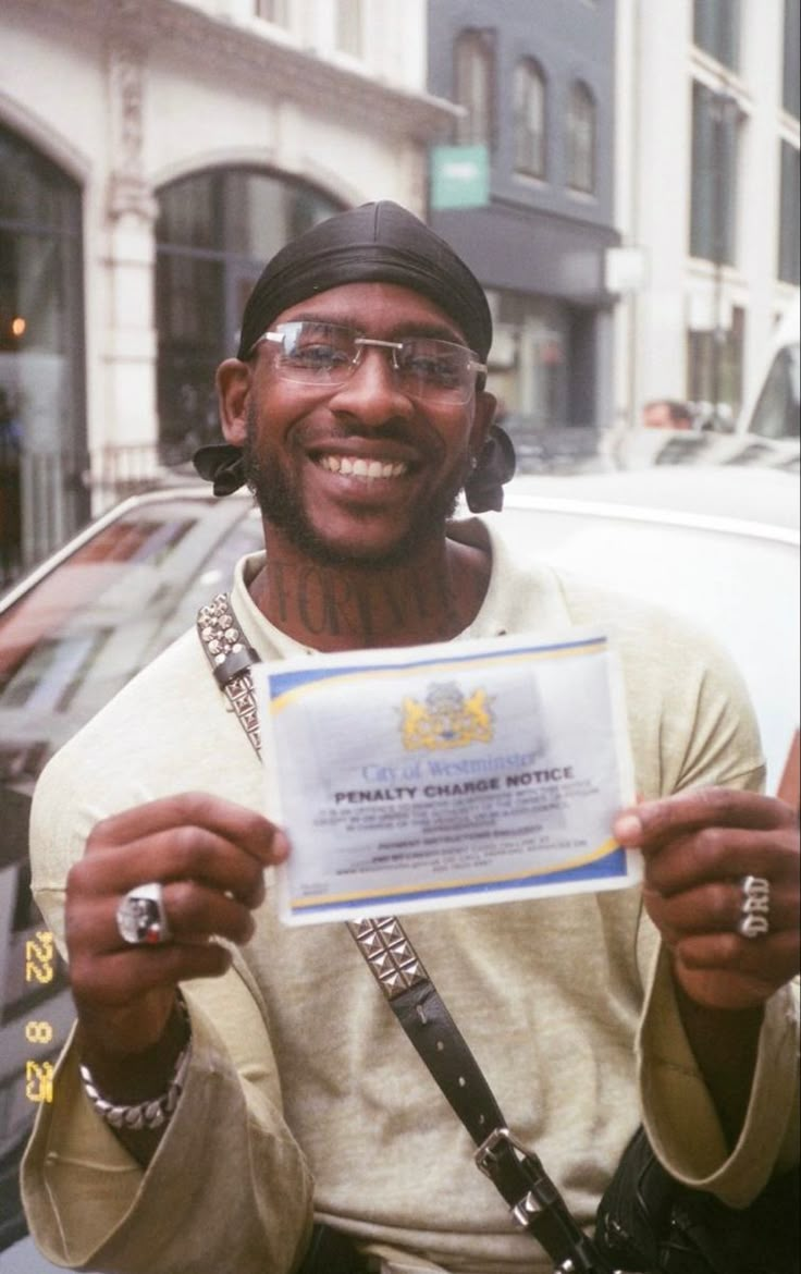 a man holding up a certificate in front of his face and wearing glasses on the street