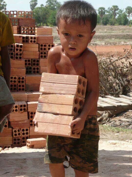 a young boy holding a block of wood in his hands and looking at the camera