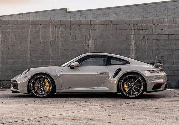 a silver porsche sports car parked in front of a brick wall on the side of a road