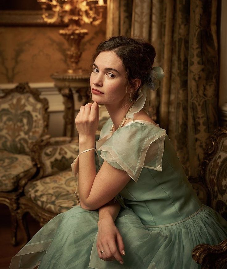 a woman in a green dress sitting on a chair with her hand under her chin