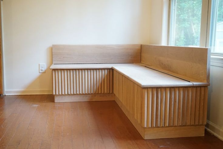 a corner bench in an empty room next to a window