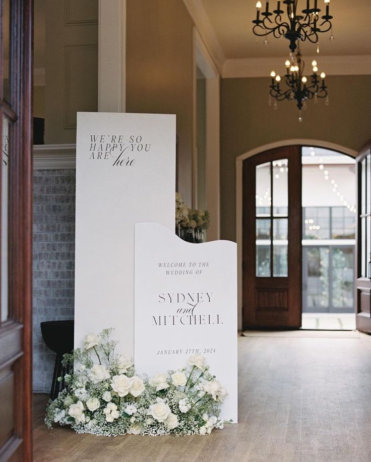 a white sign sitting on top of a wooden floor next to a chandelier