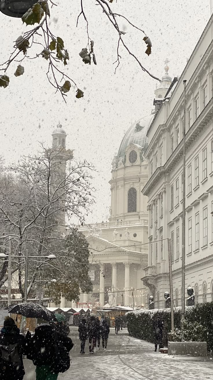 people walking in the snow with umbrellas on a city street during a snowy day