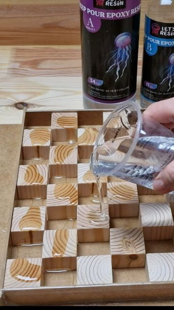 a person pouring water into a glass on top of a checkered wooden board with other items