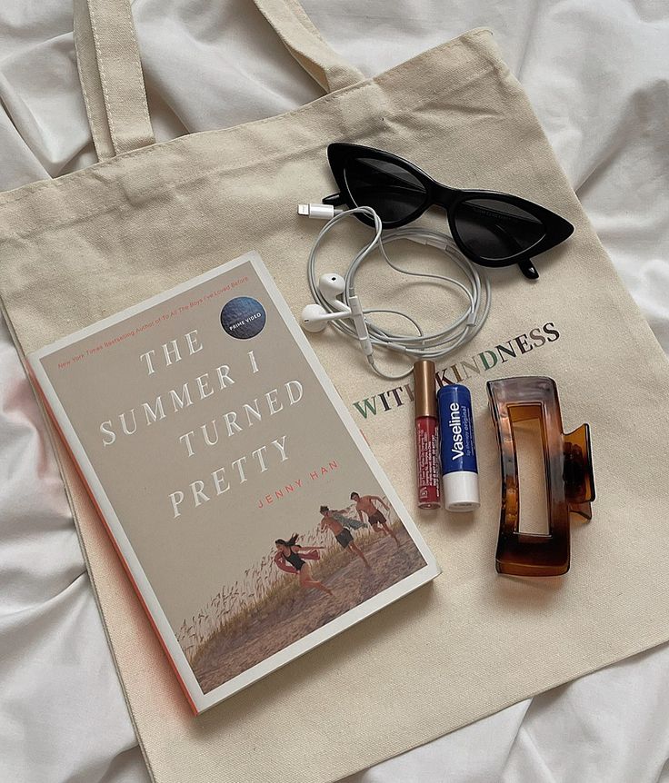 a book, sunglasses and other items are laying on a bed with a tote bag