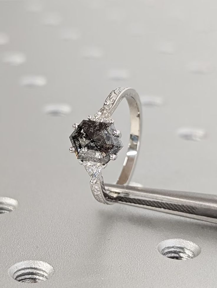 a diamond ring sitting on top of a silver surface with drops of water around it