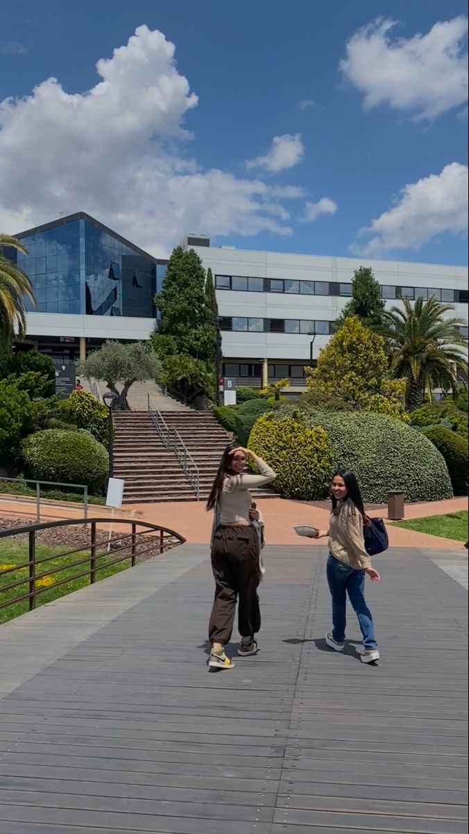 two people standing on a walkway in front of a building with stairs and palm trees