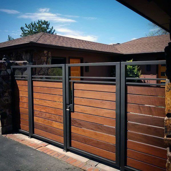 a wooden gate with metal bars on the top and bottom, in front of a house