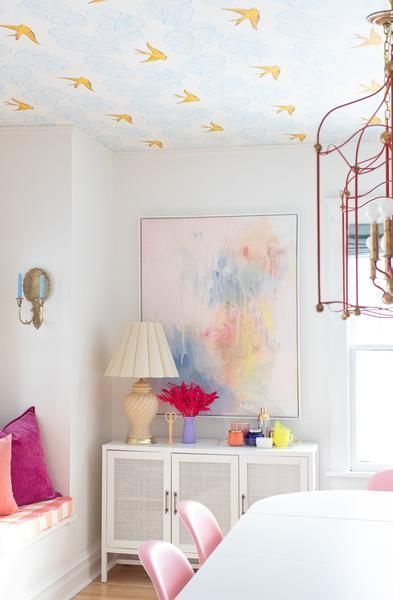 a white dining room with pink chairs and paintings on the wall