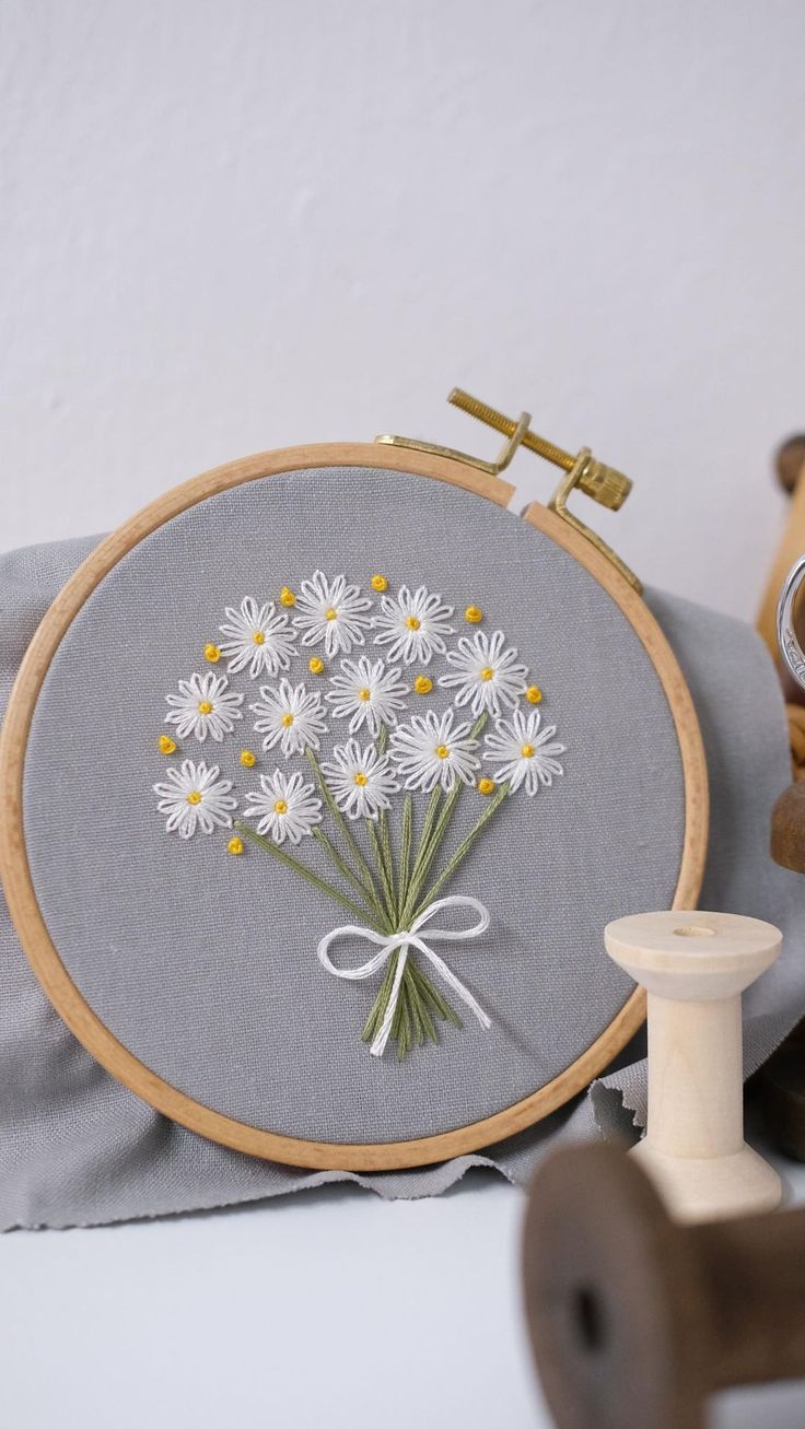 a close up of a embroidery on a pillow with flowers in the middle and a thread spool next to it