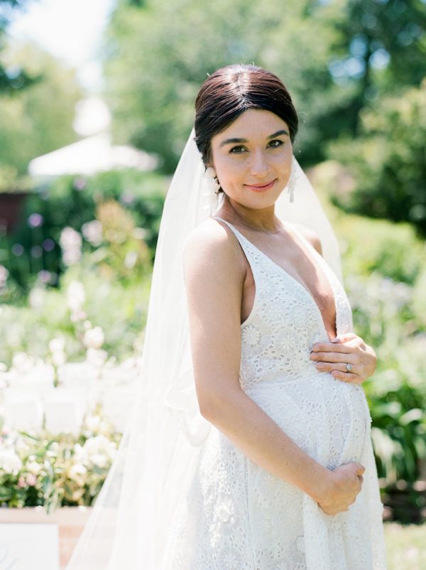 a pregnant woman wearing a wedding dress and veil poses for a photo in the garden