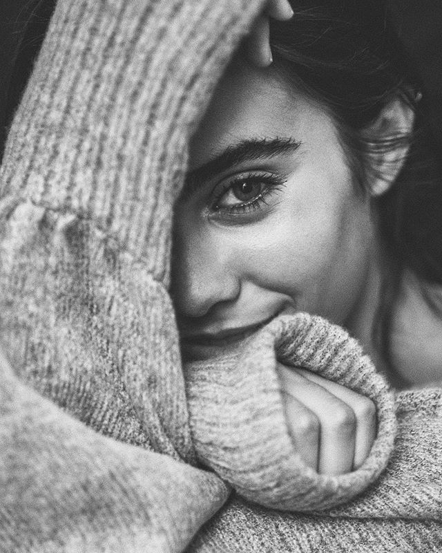 a black and white photo of a woman wrapped up in a blanket looking at the camera