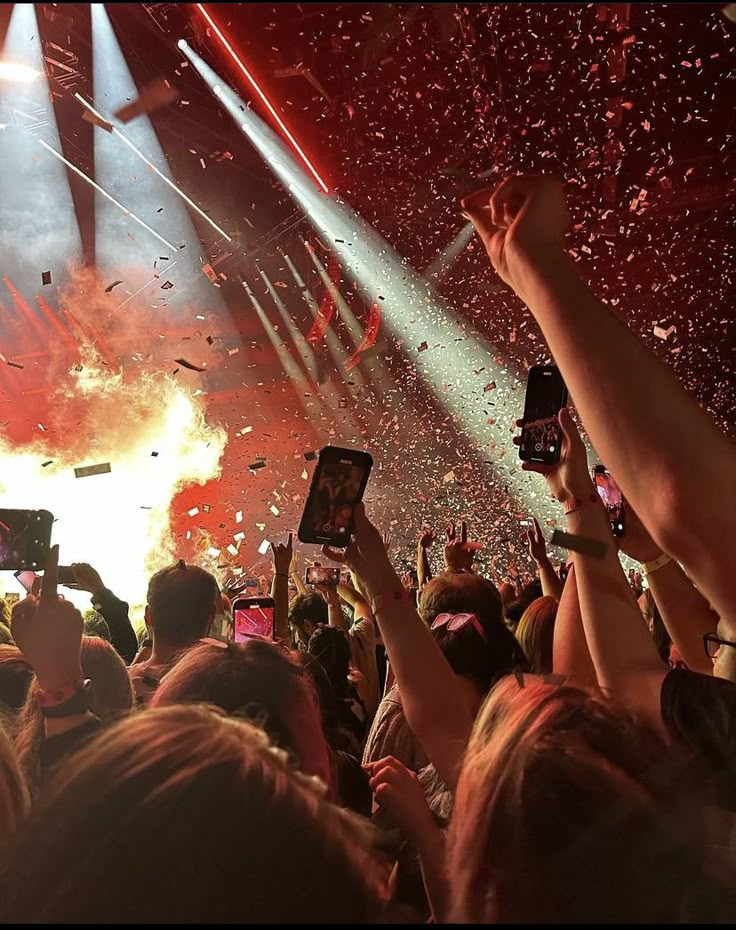 a crowd of people holding up cell phones in front of a stage with confetti