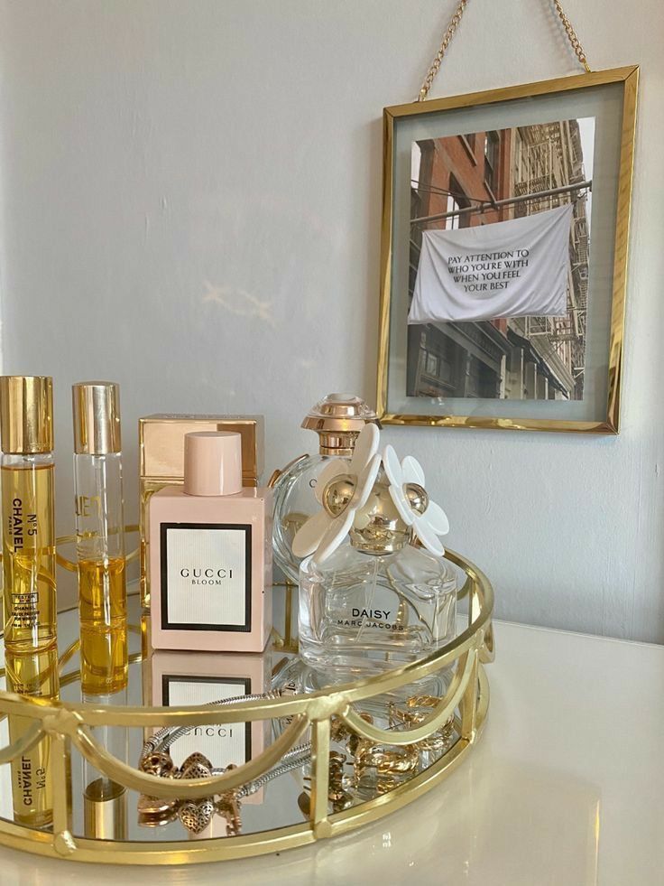 a white counter top topped with bottles of perfume and a gold tray filled with other items