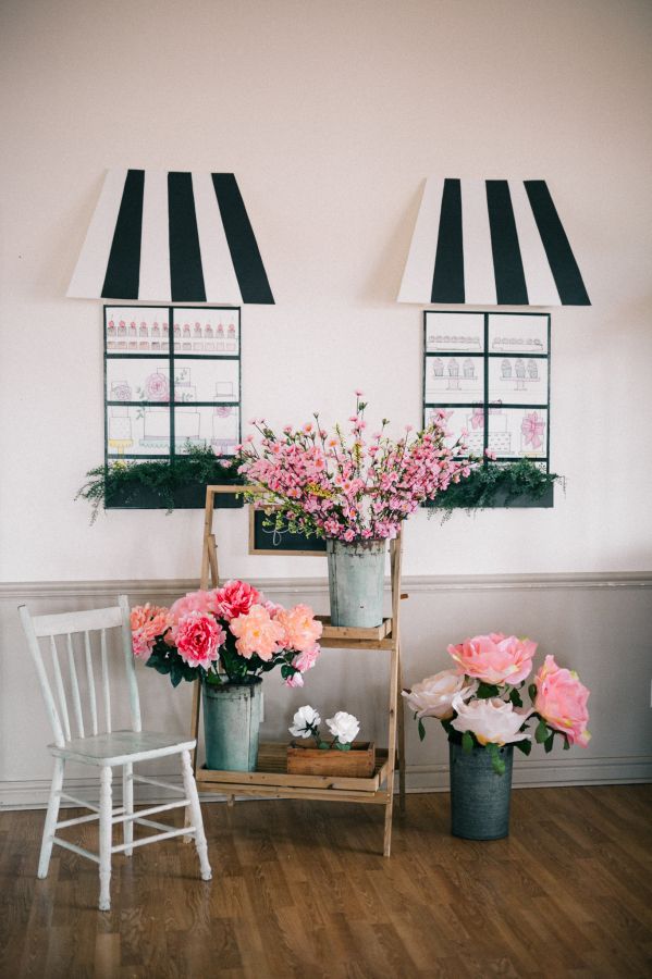 pink flowers are in buckets on a shelf next to a white chair and window