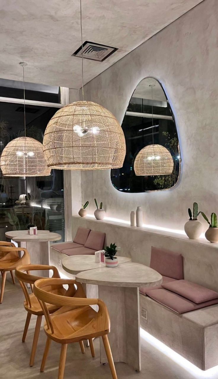 the interior of a restaurant with round tables and wooden chairs, hanging lights and circular mirrors