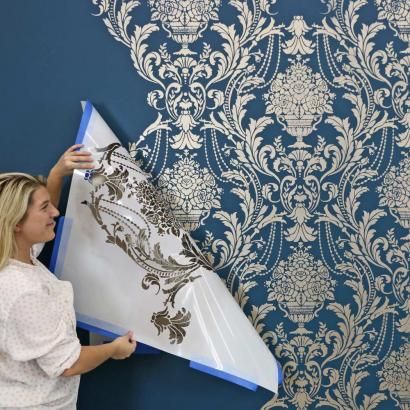 a woman is painting a wall with blue and white damask