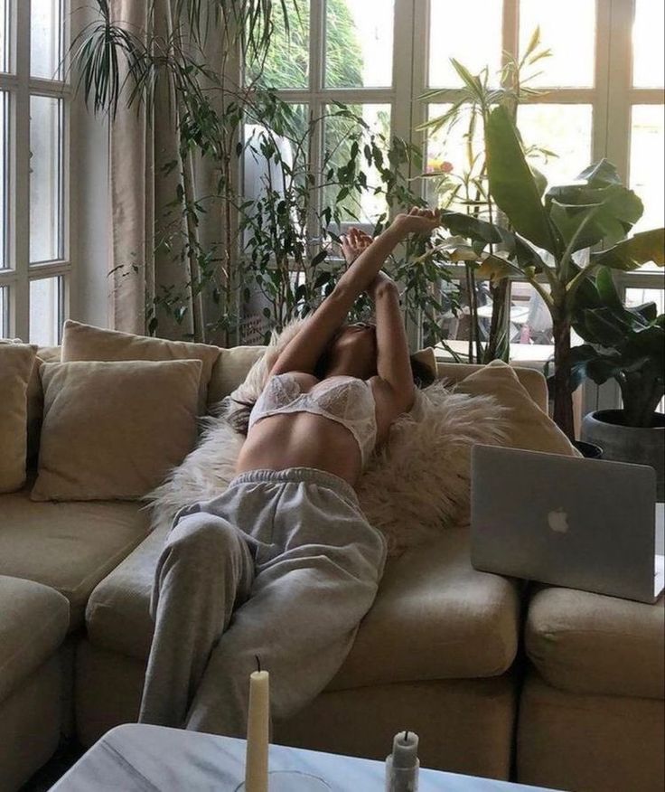 a woman laying on the couch with her legs up in the air while using a laptop