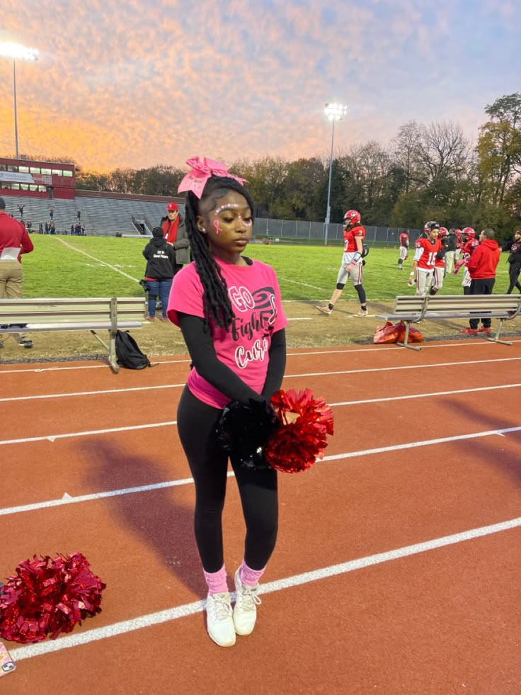 a girl in pink shirt and black pants holding cheerleader pom poms