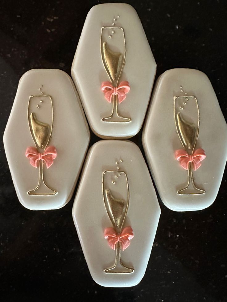 four white coasters with pink bows and champagne glasses on them, sitting on a black surface