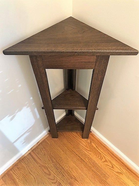 a wooden corner table sitting on top of a hard wood floor next to a white wall