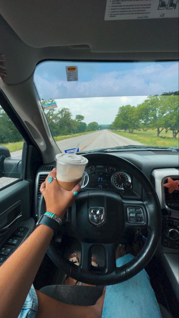 a person driving a car with a cup of coffee in their hand