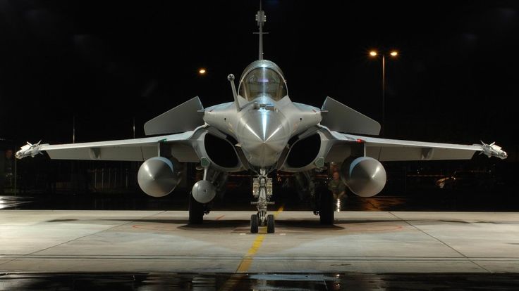 a fighter jet sitting on top of an airport tarmac at night with its lights on