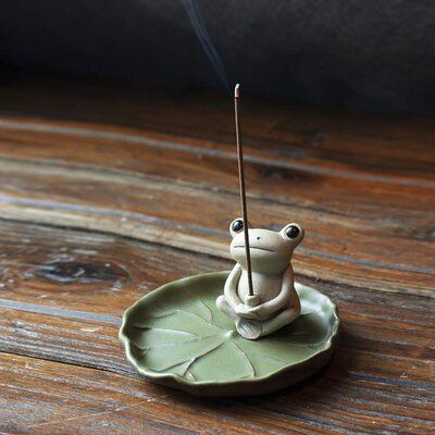 a small frog incense burner sitting on top of a leaf shaped plate with a stick sticking out of it's mouth