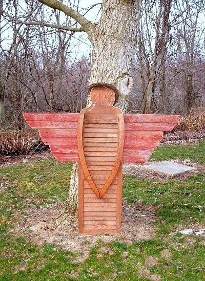 a wooden sculpture in the shape of an angel's wing on grass next to a tree