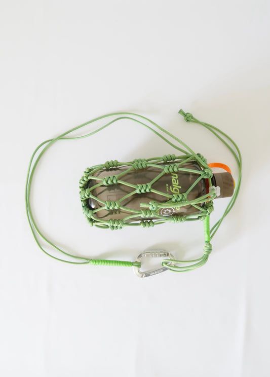 a green string wrapped around a bottle on top of a white surface with an orange cord