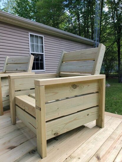 two wooden benches sitting on top of a wooden deck next to a house with trees in the background